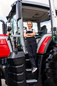 vertical portrait of female farm worker next to tractor outdoors